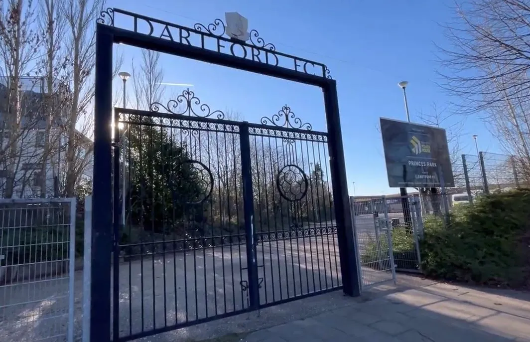 Cổng vào sân vận động Princes Park với bảng tên Princes Park Stadium, thể hiện sự đơn giản nhưng thân thiện của lối vào dành cho người hâm mộ đến xem Dartford FC thi đấu.