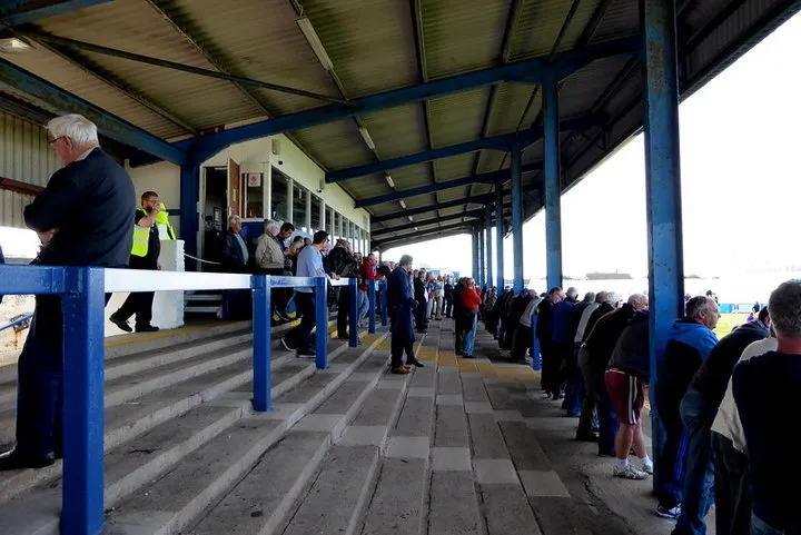 Hình ảnh các cổ động viên Barrow AFC trên khán đài bậc thang Holker Street, tạo nên không khí cổ vũ cuồng nhiệt