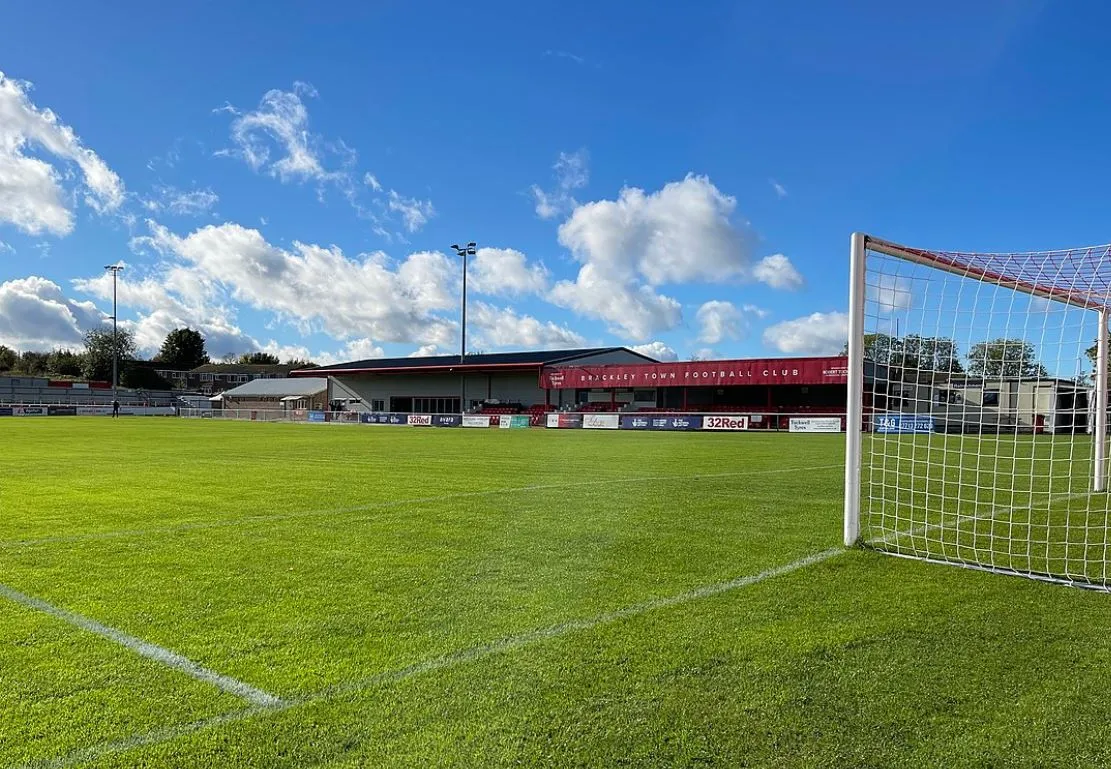 Khán đài chính St James Park Brackley với hàng ghế dành cho cổ động viên, phản ánh tinh thần bóng đá bán chuyên
