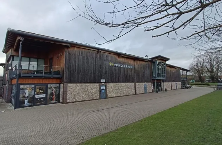 Mặt ngoài sân vận động Princes Park Dartford, lối vào chính với biển hiệu câu lạc bộ Dartford FC, cho thấy sự hòa mình vào không gian xanh của khu vực.