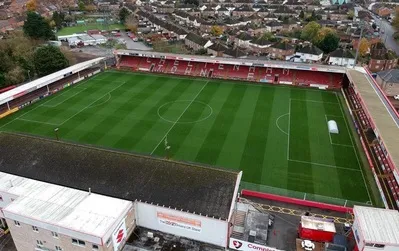 Toàn cảnh sân vận động Whaddon Road từ trên cao, nhìn rõ cấu trúc và vị trí các khán đài, biểu tượng của Cheltenham Town FC.